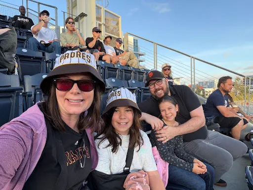 Principal Miller in company of her family wearing San Diego Padres hats in the stadium stands during a baseball game.