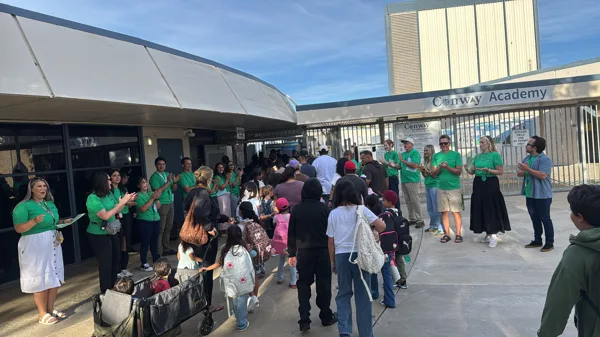 Staff in green shirts applaud and welcome students and families arriving at Conway Academy on what appears to be the first day of school.