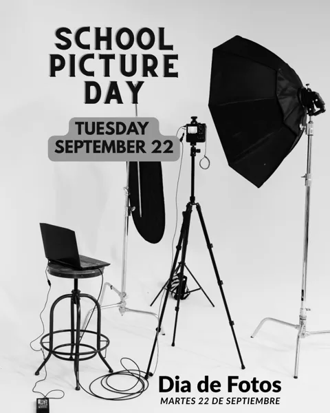 A black-and-white photo studio setup with a camera on a tripod, a large octagonal softbox light, a backdrop stand, and a stool with a laptop on it.
