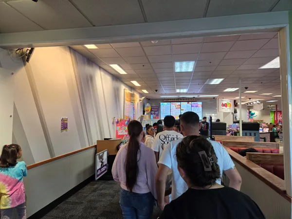 A crowd of adults and children wait in line at a Chuck E. Cheese restaurant near the order counter.