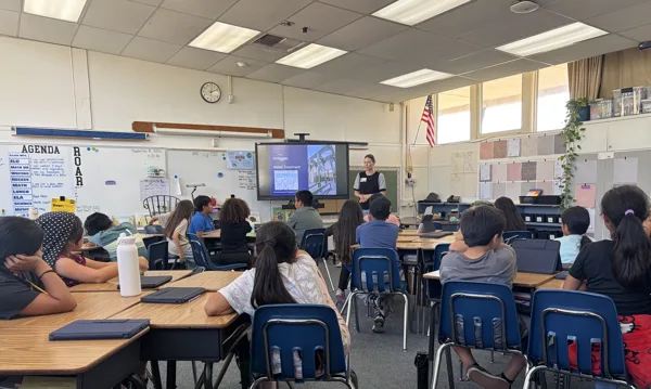 A teacher presents a Water Treatment slideshow to a classroom of elementary school students seated at desks.