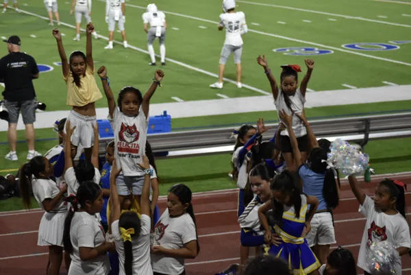 Young cheerleaders from the Felicita Cheer Team perform stunts on the sideline of a football field during a game.
