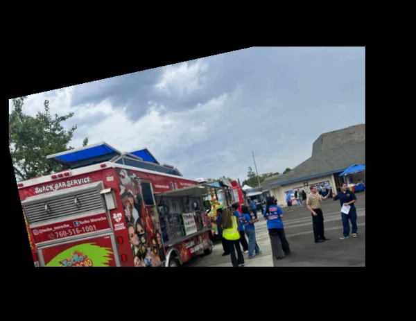 A food truck parked on a school blacktop with families and staff gathered nearby under canopies.