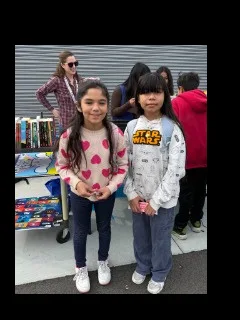 Two students standing beside a resource table with an adult volunteer behind them.