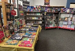 A colorful retail store displays books, games, and merchandise on yellow-clothed tables and shelving units.