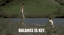 Two people are outdoors near water, one balancing on a narrow surface while the other crouches nearby watching, with the caption "Balance is key.