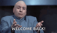 A bald man in a dark suit gestures with his hands while the text "WELCOME BACK!" appears at the bottom of the frame.