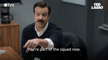 A mustachioed man in a suit points forward while sitting in an office, with the subtitle You're part of the squad now displayed, from the Apple TV+ series Ted Lasso.