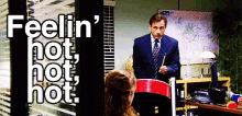 A man in a suit stands at the front of an office classroom while text on screen reads "Feelin' hot, hot, hot.