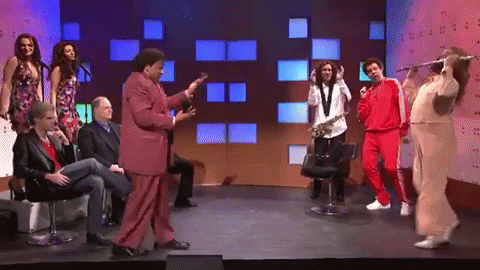 Group of people playing instruments while one man in a white suite dances across the floor playing a long flute