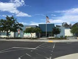 A large modern commercial or civic building with an American flag and California state flag flying out front on a clear sunny day.